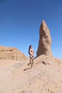 Rear view of man standing on rock against clear blue sky