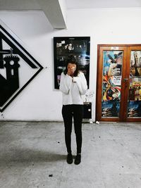 Full length portrait of woman standing against wall