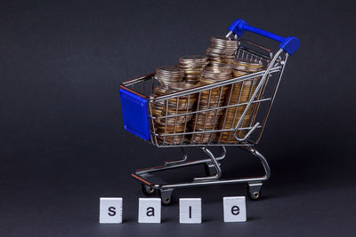 Close-up of coins in small shopping cart against gray background