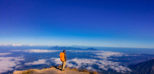Rear view of man standing on mountain against blue sky