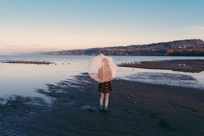 Rear view of woman standing on beach against sky