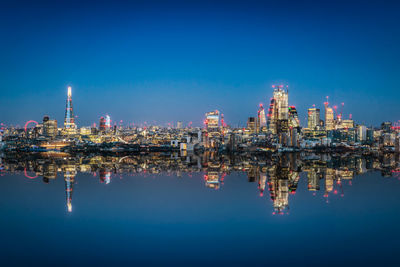 Reflection of illuminated buildings in lake against blue sky