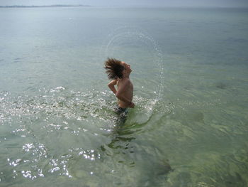 Shirtless boy splashing water from wet hair in sea