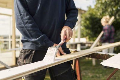 Man painting wooden plank while woman assisting in background