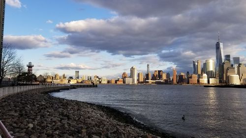 City at waterfront against cloudy sky