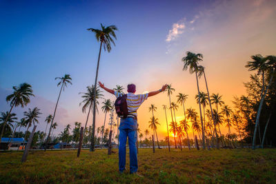 Rear view of man standing by palm trees on field against sky