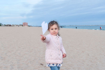 Cute young girl is playing with paper airplanes on the beach