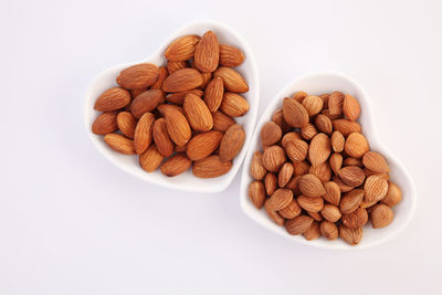 Close-up of almonds in heart shape bowls over white background
