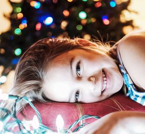 Portrait of cute girl lying down amidst illuminated christmas lightings