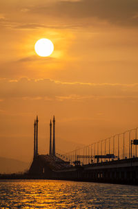 Silhouette bridge over sea against sky during sunset