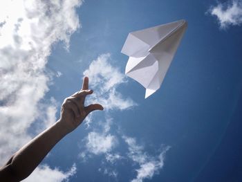 Cropped hand of person by paper airplane against sky