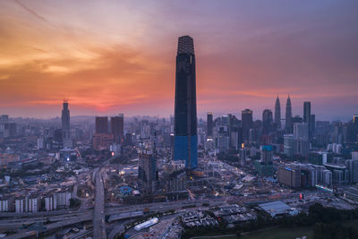 Illuminated modern buildings in city against sky during sunset