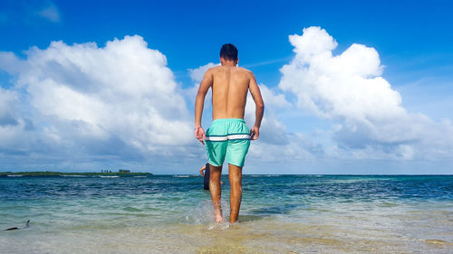 Rear view of shirtless man wading in sea against sky