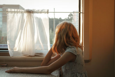 Side view of woman standing by window at home