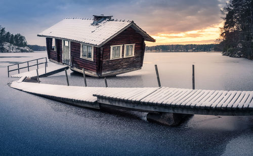 Sauna cottage by lake against sky during sunset with pier
