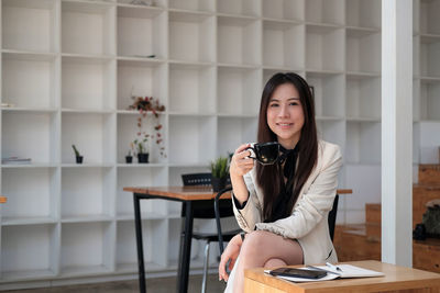 Portrait of young woman using mobile phone while sitting on table