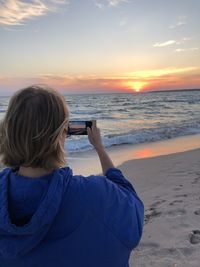 Rear view of woman photographing sea against clear sky