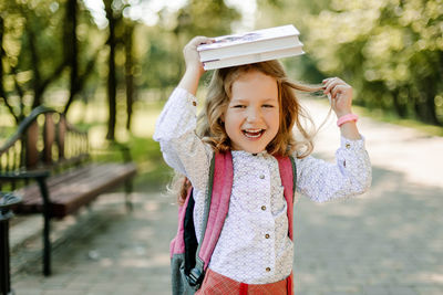 A charming little girl with a book on her head, on the first day at school or kindergarten. 
