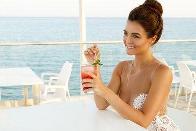 Beautiful woman sitting at restaurant against sea