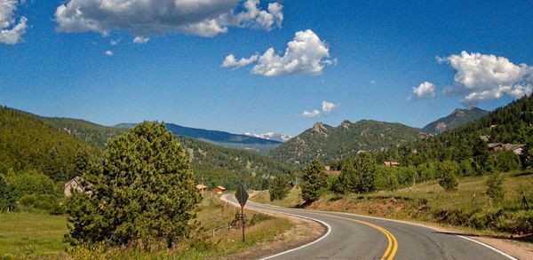 Road amidst trees and mountains against sky