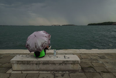 Rear view of woman on retaining wall by sea against sky