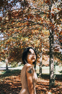 Side view of young woman standing against trees