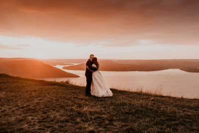 Rear view of woman standing on field against sky during sunset