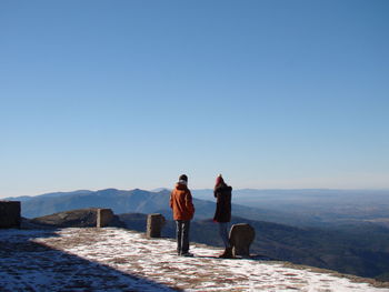 Rear view of people standing on snow against clear sky