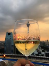 Close-up of hand holding wineglass against sky during sunset