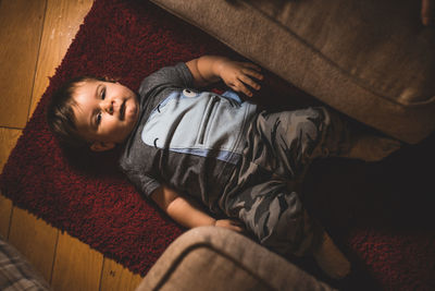 High angle portrait of cute boy lying down on carpet at home