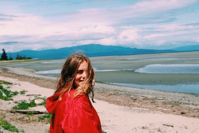 Happy young woman standing at beach against cloudy sky