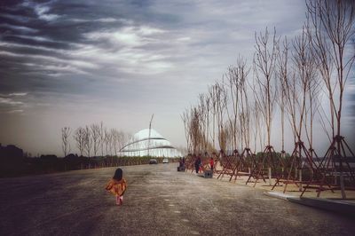 Rear view of girl running on street against sky