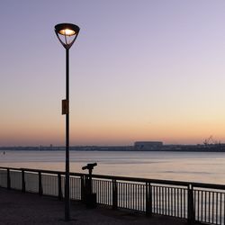 Street light by sea against sky during sunset