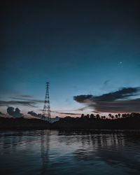 Electricity pylon by river against sky during sunset