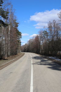 Empty road along trees and against sky