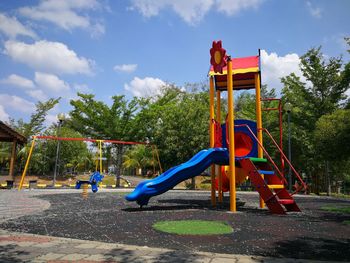 Children playing on slide at park against sky