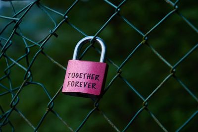 Close-up of lock with text on chainlink fence