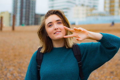 Portrait of smiling young woman gesturing while standing outdoors