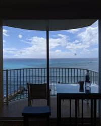 Chairs and table by sea against sky seen through window