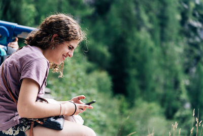 Young woman using mobile phone while sitting on tree