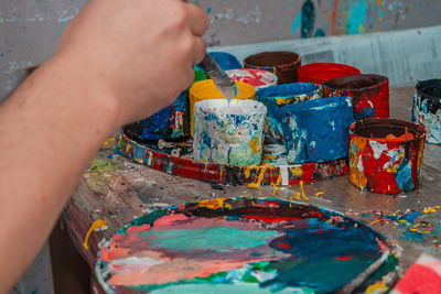 The artist's hand with a brush reaches for the jars of paints in the art studio