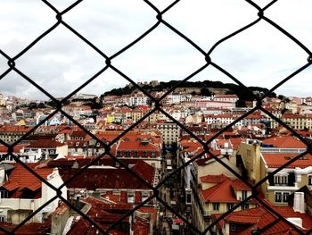 Cityscape against sky seen through chainlink fence