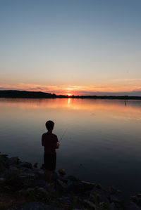 Adolescent boy fishing on shore of lake at sunset in ontario, canada.