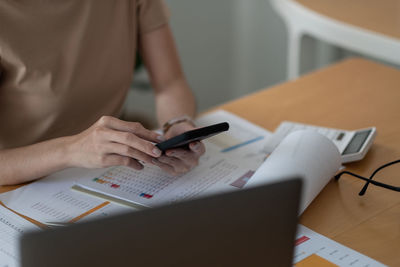 Midsection of woman using smart phone on table