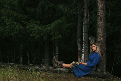 Young woman sitting on tree trunk in forest