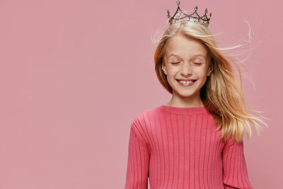 Portrait of young woman standing against pink background