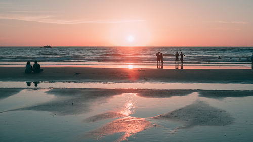 Silhouette people on beach against sky during sunset