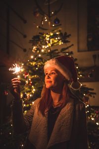 Portrait of smiling young man in illuminated christmas tree at night