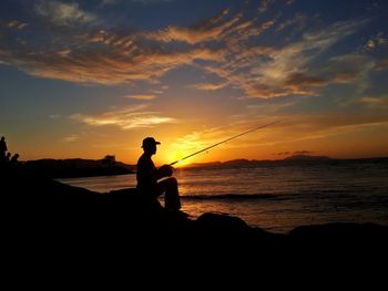 Silhouette man fishing on beach against sky during sunset