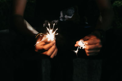 Midsection of person holding illuminated sparklers at night